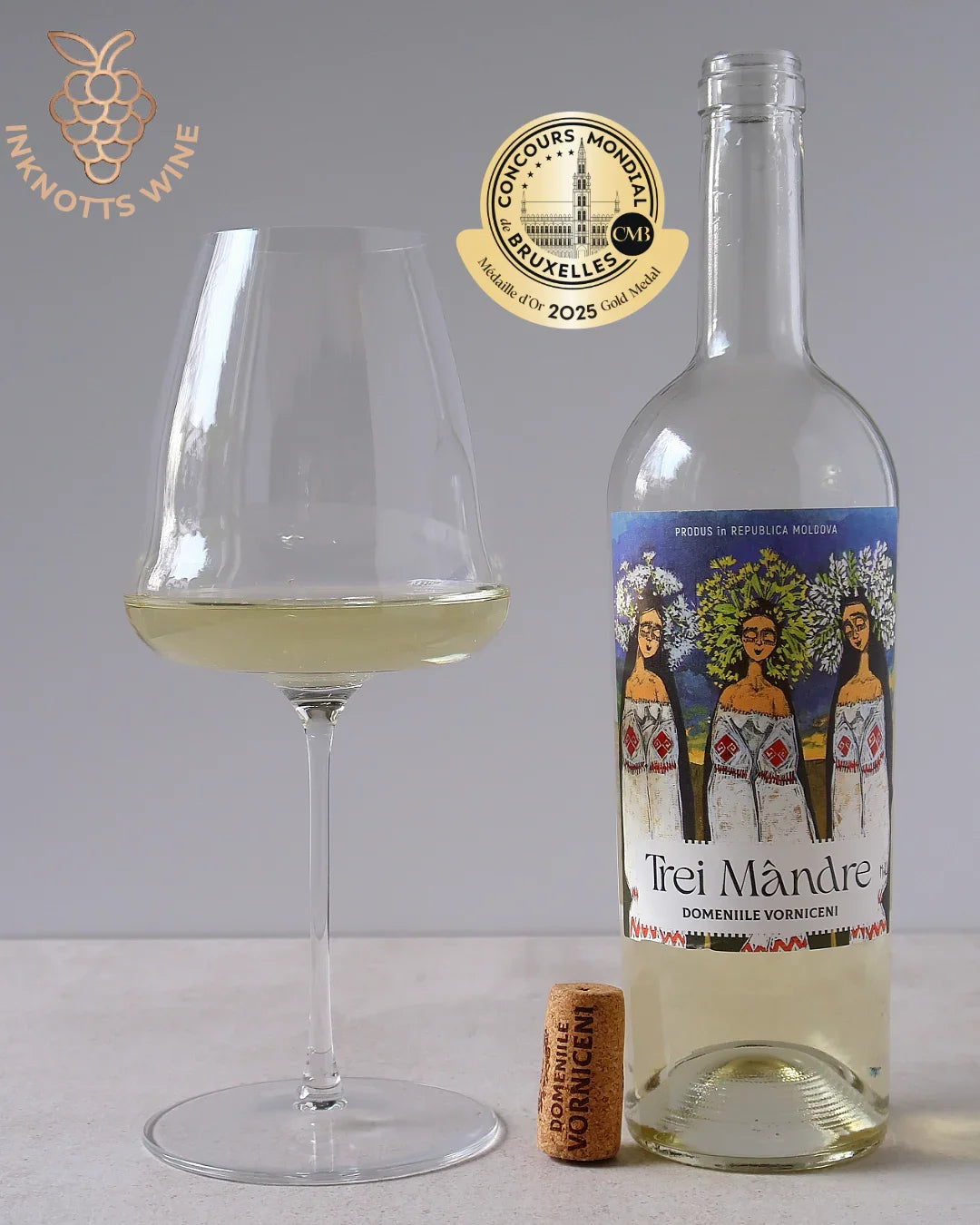 Moldovan white wine bottle labeled Trei Mândre with filled glass, cork, and gold award badge