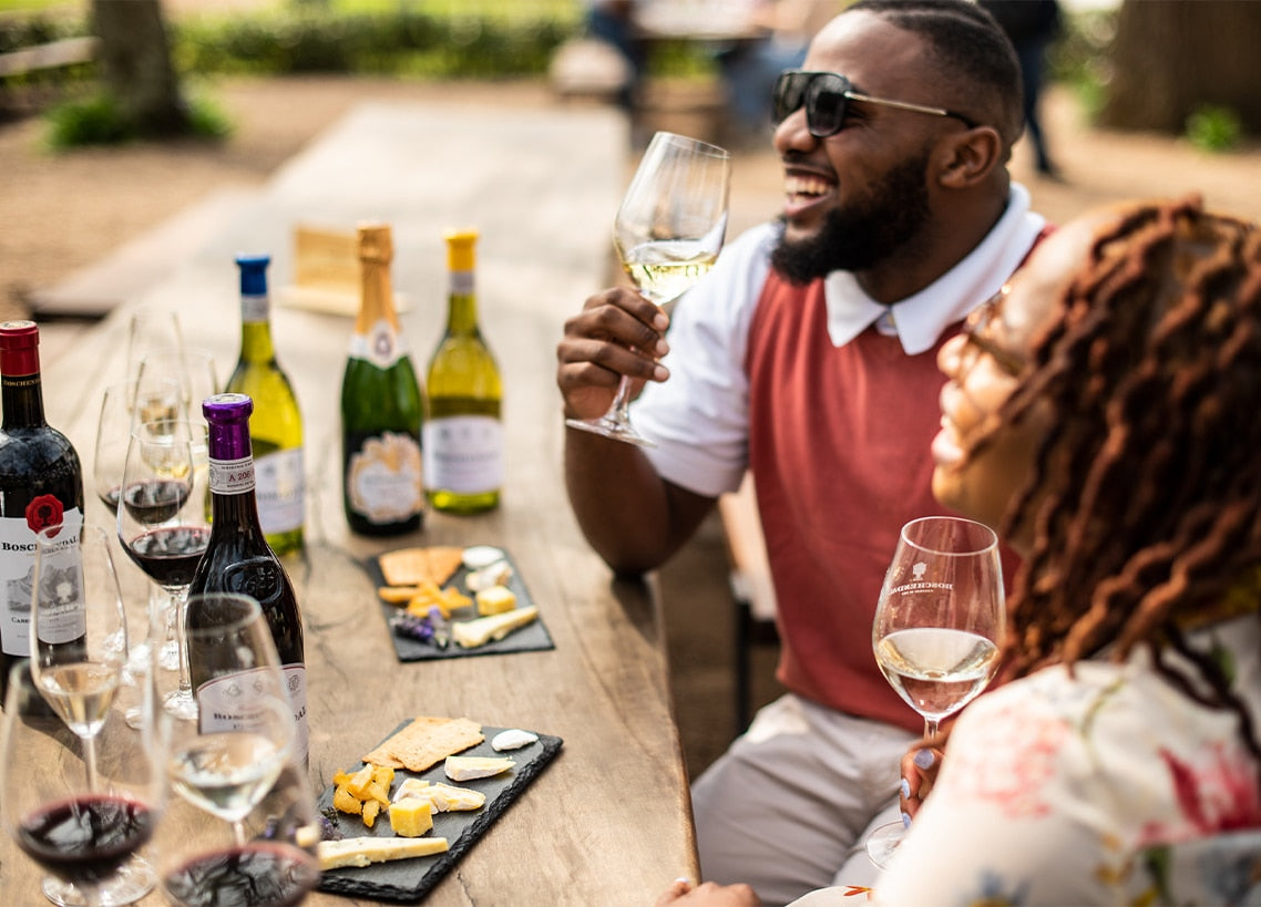 Two people enjoying wine and cheese at an outdoor table.